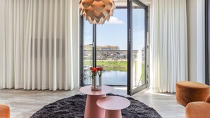A modern living room with a large window, a unique pendant light, a round table with a vase of flowers, and a black rug. - Apartment Kamperland With Harbour View (Kamperland)