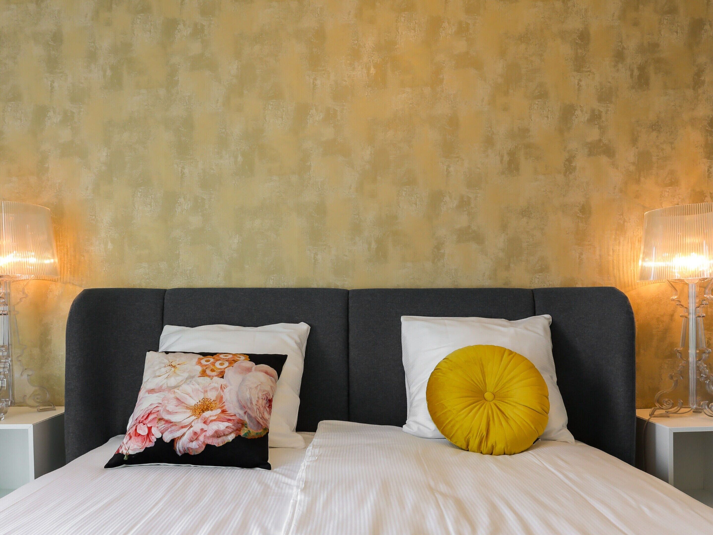 Una cama bien hecha con dos almohadas, una lámpara de noche y una pared con textura.