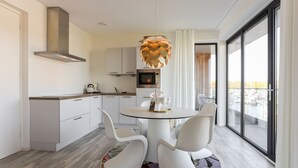A modern kitchen with white cabinets, a round dining table with white chairs, and a view of a marina through large windows. - Apartment Kamperland With Harbour View (Kamperland)
