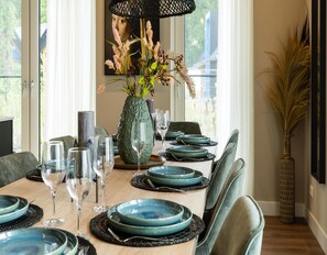 A dining table set with blue plates, clear wine glasses, and a green vase with dried flowers. - Veluwe Villa Wellness (Wekerom)