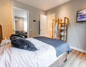 A bedroom with a bed, a wooden wardrobe, a television, and a bathroom visible through an open door. - Veluwe Villa Wellness (Wekerom)