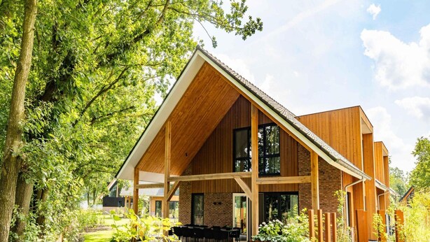 Une maison moderne dotée d’un grand porche, de poutres en bois et d’une façade en briques.