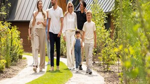 Une famille se promène sur un chemin pavé, bordé de verdure et entourée de bâtiments modernes aux toits inclinés.