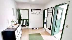 A hallway with a wooden floor, a green mat, a black cabinet, and a mirror on the wall. - Uitzicht op Staufen (Piding)
