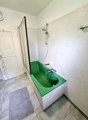A bathroom with a green bathtub, a shower, a white door, and a clock on the wall. - Uitzicht op Staufen (Piding)