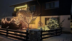 A house with a stone wall and a wooden fence, surrounded by snow-covered plants and trees. - Uitzicht op Staufen (Piding)