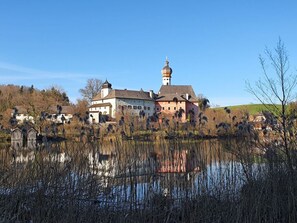 A historic building with a prominent tower, surrounded by a body of water and sparse vegetation. - Uitzicht op Staufen (Piding)