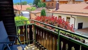A balcony with a view of a village, a table with chairs, and a railing with plants. - Uitzicht op Staufen (Piding)