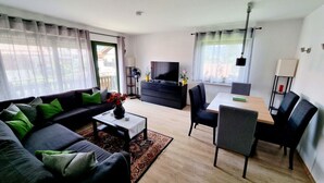 A modern living room with a sofa, coffee table, TV, and dining area. - Uitzicht op Staufen (Piding)