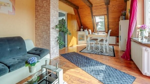 A cozy living area with a stone pillar, wooden ceiling beams, a sofa, a dining table with chairs, and a kitchen area with a refrigerator. - Apartment in Holstein With Balcony (Ploen)