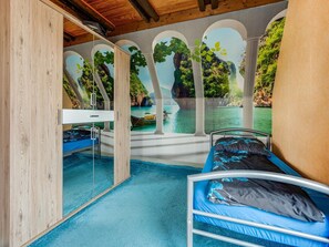 Una habitación con cama, escritorio y vistas a un paisaje costero a través de ventanales arqueados.