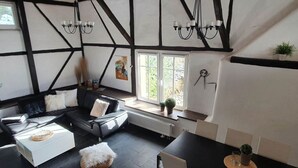 Uma sala de estar moderna com um sofá de couro preto, um banquinho branco e uma área de jantar com uma mesa preta e cadeiras brancas.