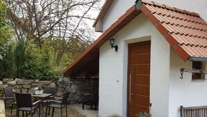 Uma casa pequena com porta de madeira, parede de pedra e um alpendre com cadeiras e mesa.