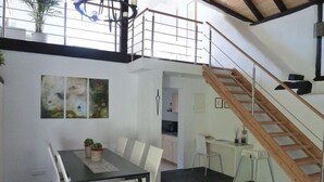 Uma área de refeições com uma mesa, cadeiras, uma escada e uma cozinha.