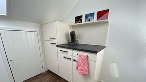 A compact kitchen with white cabinets, a black countertop, and a coffee maker. There is a small shelf with pictures above the counter. - Spacious Holiday Home Near Ski-lift (Todtmoos)