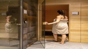 A woman in a towel exiting a room with a glass door, a sauna sign, and a wooden wall. - Comfortable Apartment With air Conditioning (Bruges)