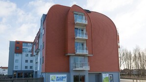 A modern building with a curved facade, multiple balconies, and a sign advertising holiday suites. - Comfortable Apartment With air Conditioning (Bruges)