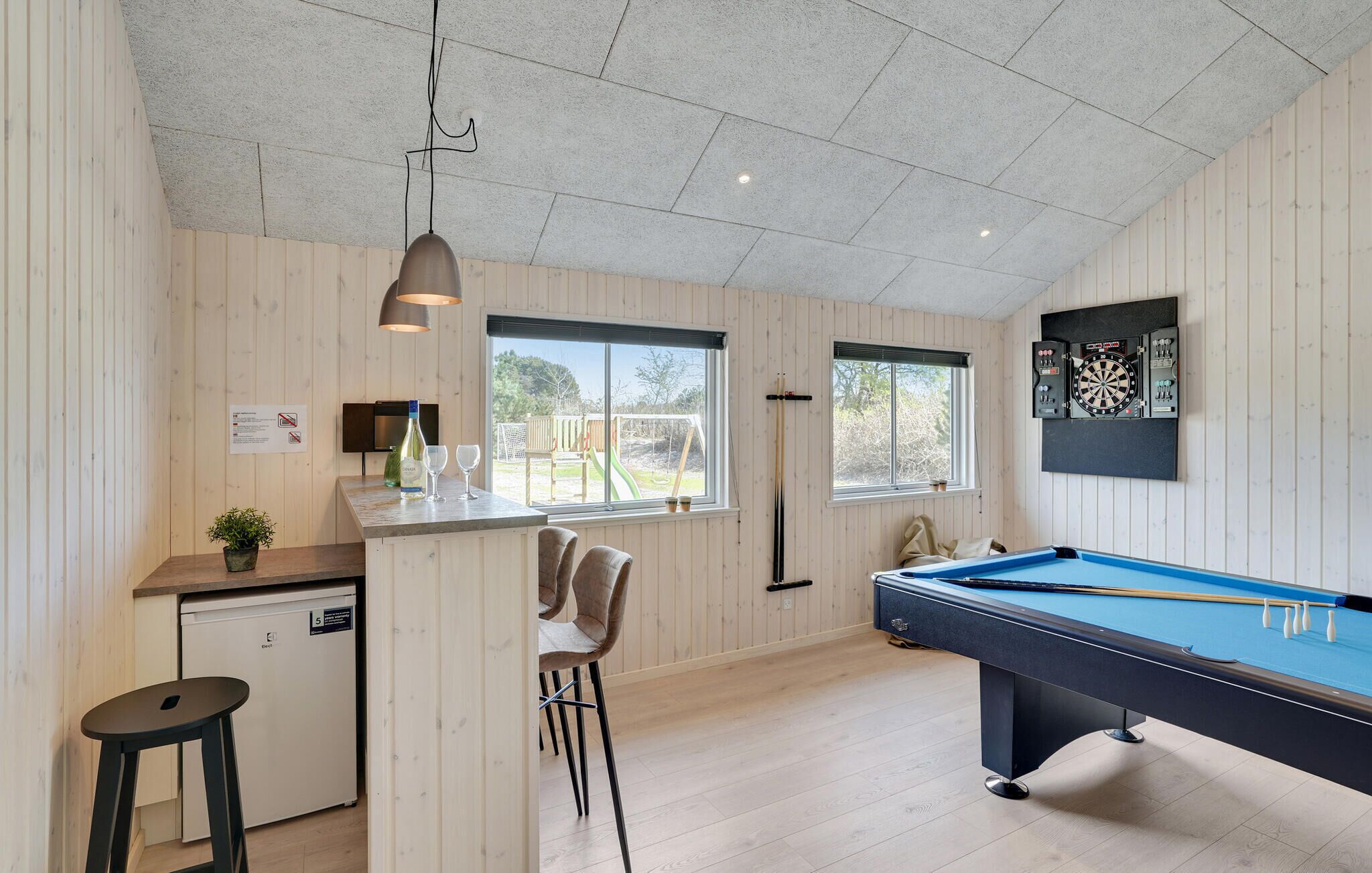 Una habitación con mesa de billar, zona de bar y pequeña cocina.