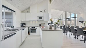 Een moderne keuken met witte kasten, een inbouwoven en een eethoek met een grote tafel en stoelen.
