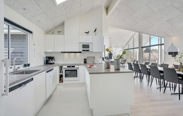 A modern kitchen with white cabinetry, a built-in oven, and a dining area with a large table and chairs. - Nice home in Væggerløse with sauna (Væggerløse)