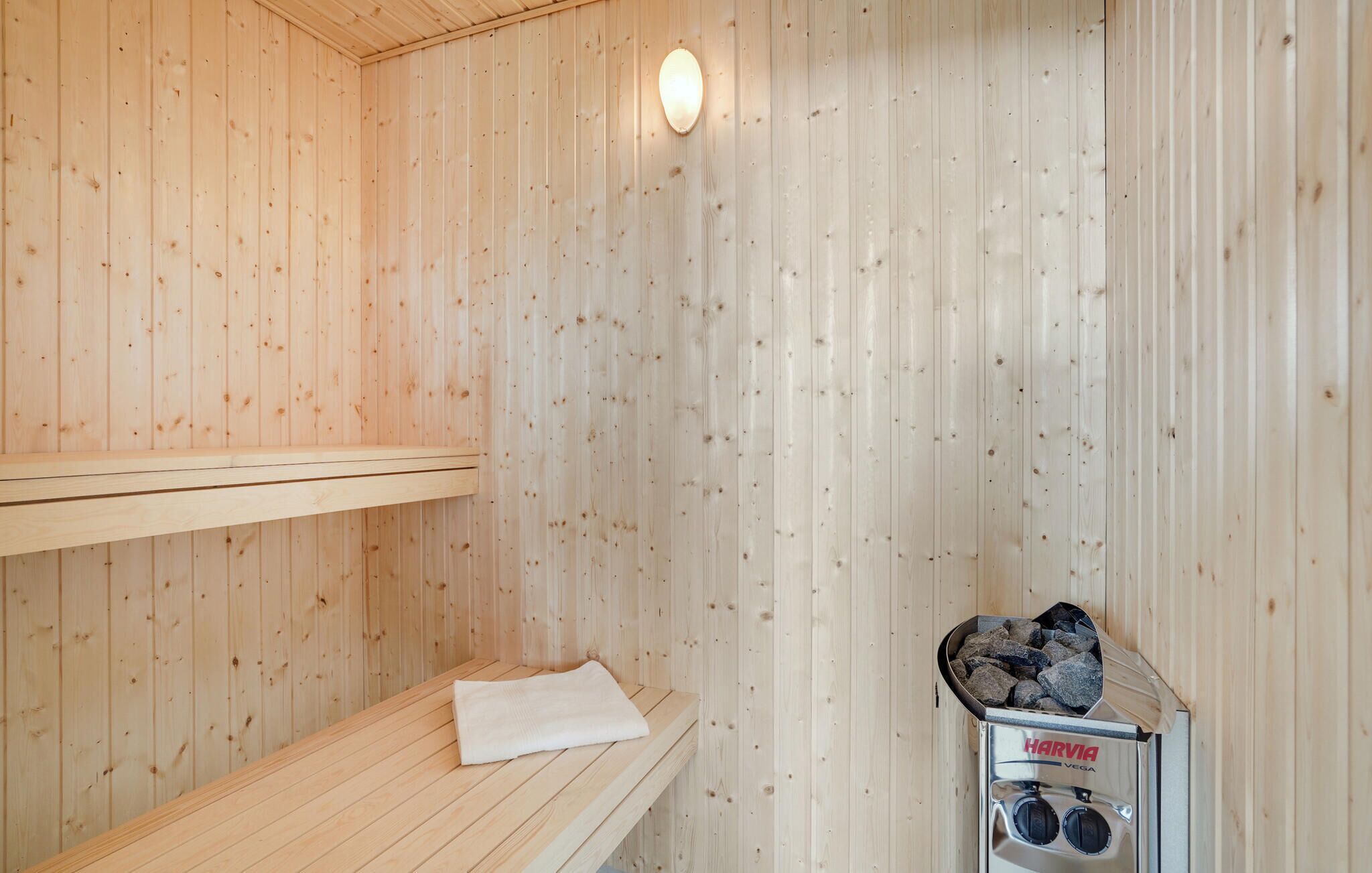 Een sauna met houten wanden, een bankje, een handdoek en een sauna-oven met de aanduiding 'HARVIA VESA'.