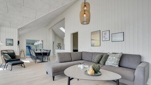 Een moderne woonkamer met een grijze modulaire bank, een ronde salontafel en een eethoek met een witte tafel en stoelen.