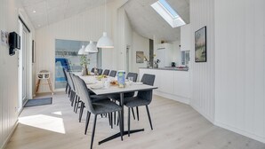 Een moderne eetruimte met een lange tafel, meerdere stoelen, hanglampen en uitzicht op de keuken.