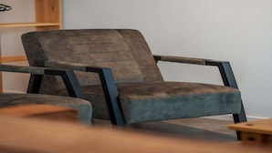 Ein moderner Sessel mit dunkler Stoffbespannung und Metallgestell, platziert in einem Raum mit Holzregal und einem kleinen Holztisch.