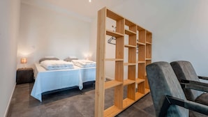 Ein Hotelzimmer mit zwei Betten, einem Holzschrank, einem grauen Sessel und einem Nachttisch mit Lampe.
