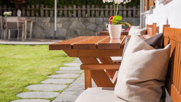 A wooden bench with a cushion, a picnic table, and a potted plant with flowers. - Apartment in St. Jakob im Ahrntal Sudtirol (Valle Aurina)