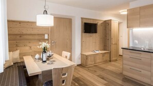A modern kitchen with wooden cabinetry, a dining area with a table and chairs, and a television mounted on the wall. - Apartment in St. Jakob im Ahrntal Sudtirol (Valle Aurina)