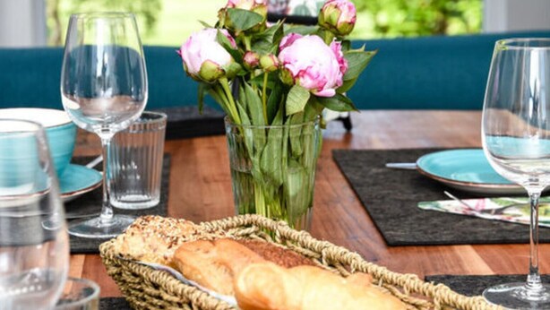 A dining table with a basket of bread, a vase of flowers, and wine glasses. - Holiday Apartment Elbe (Drochtersen)
