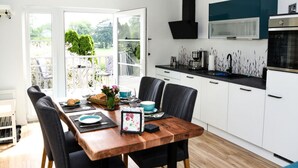 A modern kitchen with white cabinets, a wooden dining table, and black chairs. - Holiday Apartment Elbe (Drochtersen)