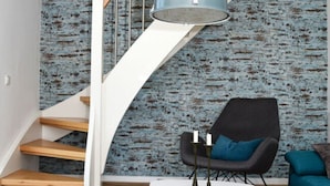 A modern living room with a staircase, a round white table with two candles, a black armchair, and a teal sofa. - Holiday Apartment Elbe (Drochtersen)