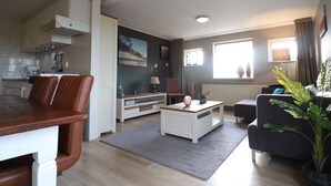 A modern living room with a dining area, a kitchen, and a large window providing natural light. - Holiday Home in Donkerbroek Near Forest Trails (Donkerbroek)