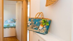 A hallway with a bed in the background, a wicker basket on a shelf, and a blue basket with decorative elements. - Apartment 3 Beaches With Free Parking (Dubrovnik)