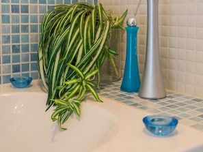 Une salle de bain avec un lavabo blanc, des murs recouverts de carreaux bleus et blancs, un distributeur de savon bleu et un récipient en verre contenant une plante.