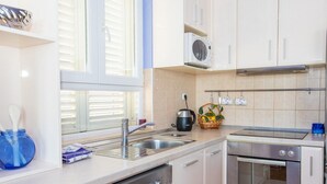 A modern kitchen with white cabinets, a Bosch dishwasher, a built-in oven, and a window with blinds. - Apartment 3 Beaches With Free Parking (Dubrovnik)