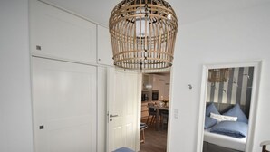 A bedroom with two beds, a wooden ceiling light fixture, and a view of a dining area. - Watt`n Flair on the North Beach (Borkum)