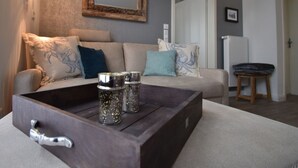 A modern living room with a sofa, decorative pillows, a wooden coffee table with glass jars, and a wall-mounted mirror. - Watt`n Flair on the North Beach (Borkum)