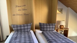 A hotel room with two single beds, each with a checkered duvet and pillows. A wooden panel with text is on the wall, and a small table with a lamp is visible. - Huis Rieslehof Vakantiewoning 11 (Titisee-Neustadt)