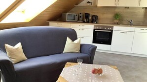 A cozy living area with a dark blue sofa, a small wooden table with a white tablecloth, and a kitchen in the background. - Huis Rieslehof Vakantiewoning 11 (Titisee-Neustadt)