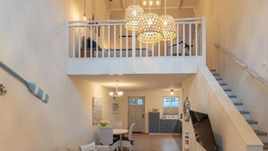 A spacious interior with a dining area, kitchen, and a staircase leading to a loft. - Fordebrise Modern Retreat (Steinberg)