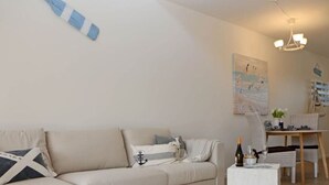 A living room with a sofa, a small table with a bottle and glass, and a dining area with a chair and table. - Fordebrise Modern Retreat (Steinberg)