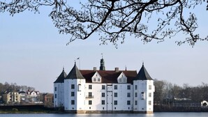 A large white building with multiple towers and a flag, situated by a body of water. - Fordebrise Modern Retreat (Steinberg)