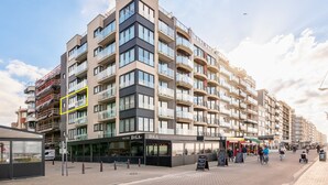 A multi-story building with balconies, a restaurant named "DiGA Food & Drinks," and a visible storefront. - Apartment in Koksijde With Sea Views (Koksijde)