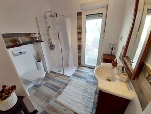 Un bany amb dutxa, vàter, rentapel i una petita finestra.