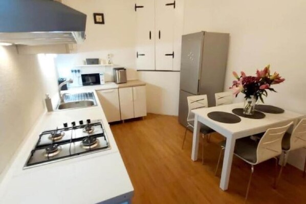Una cuina compacta amb fogó de gas, armaris blancs, microones i nevera.
