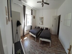 A room with two beds, a ceiling fan, a window with curtains, and a floor lamp.