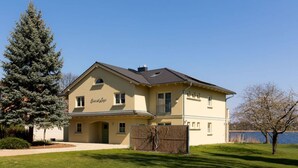 A two-story house with a large front yard, a wooden fence, and a tree. - Casa sul Lago Modern Retreat (Werder (Havel))